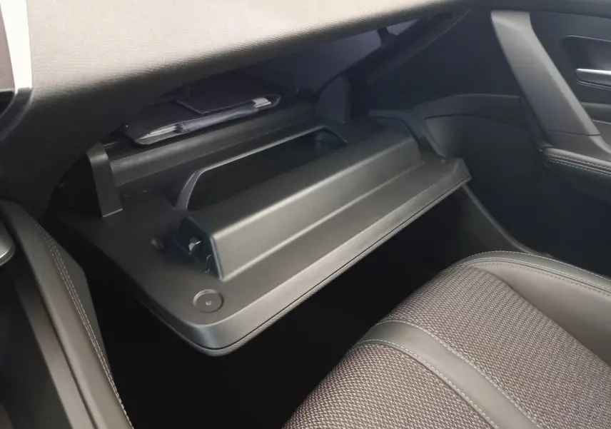 Intérieur de la Peugeot 308 2022, vue côté passager sur la boîte à gants ouverte et siège tissu gris.