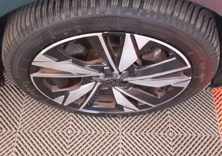 Gros plan sur la jante alliage noire et argentée d’une Peugeot 308 bleu, mettant en valeur le logo central.