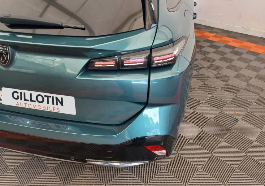 Vue arrière droite d'une Peugeot 308 bleu métallisé avec feux arrière LED et logo Peugeot visible.