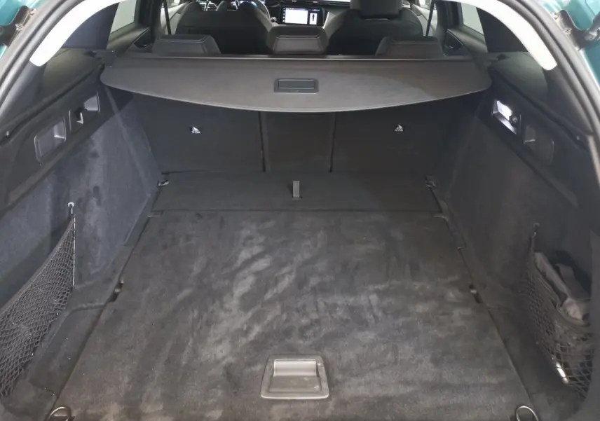 Vue de l'intérieur du coffre spacieux et noir de la Peugeot 308 bleu, avec banquette arrière rabattue et cache-bagages.