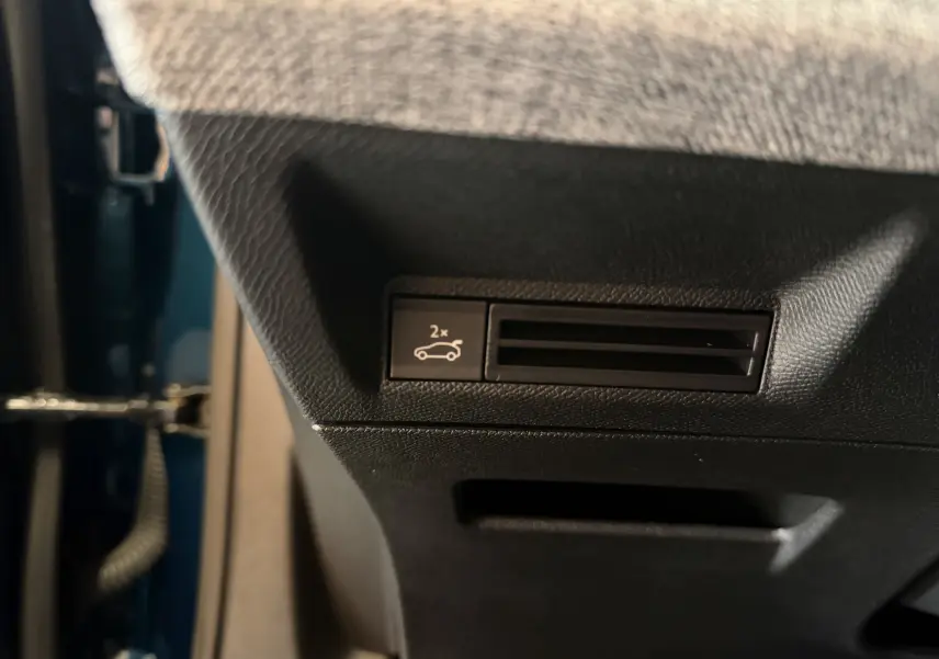 Détail intérieur du bouton d'ouverture du hayon sur la partie inférieure côté conducteur du Peugeot 3008 Hybrid 145 GT bleu obsession.