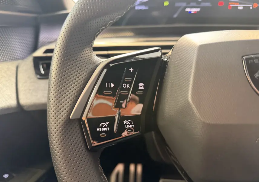Gros plan sur le côté gauche du volant perforé du Peugeot 3008 Hybrid 145 GT avec commandes intégrées et finition noire.