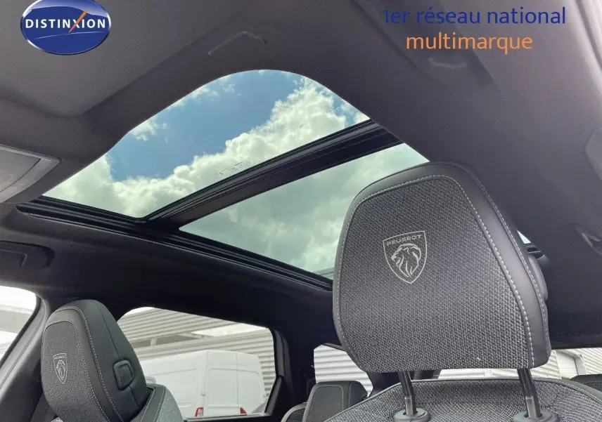 Vue intérieure du Peugeot 5008 Hybrid 2025, toit panoramique ouvert et appuie-tête avant en tissu noir avec logo brodé.