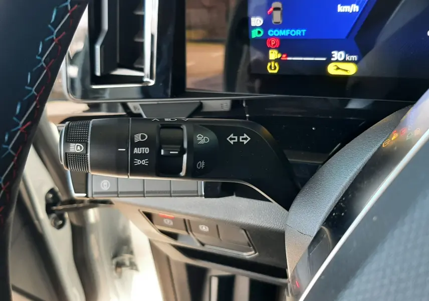 Gros plan sur la commande des feux et clignotants côté gauche du volant d’un Renault Austral blanc nacré, tableau de bord digital visible.