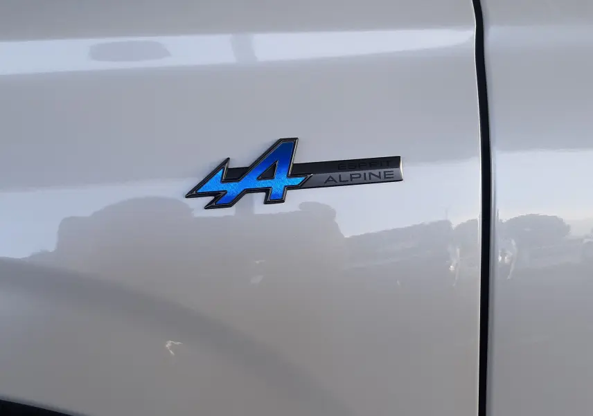 Gros plan sur l'écusson bleu "Esprit Alpine" sur la porte blanche nacrée du Renault Austral 2025.