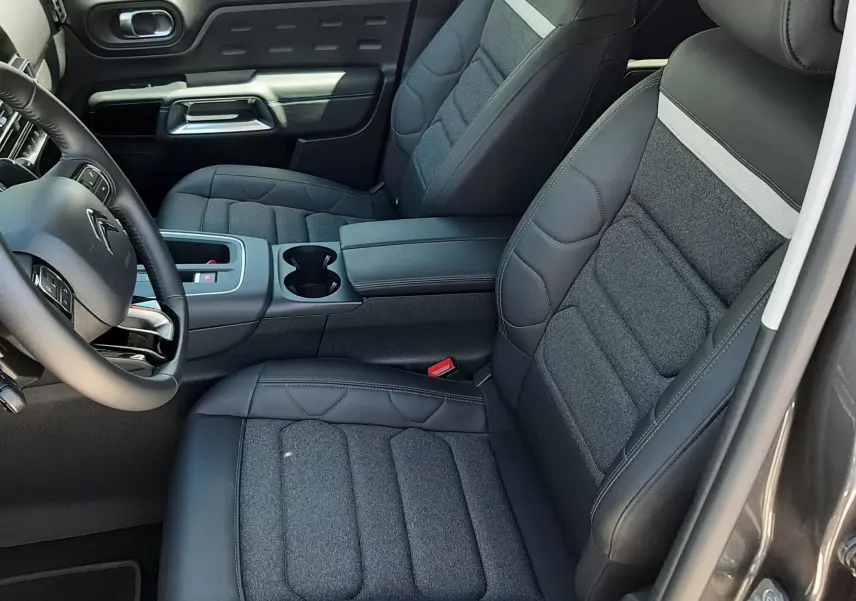 Vue intérieure côté conducteur du Citroën C5 Aircross hybride 2025, sièges tissu et cuir noir avec surpiqûres grises.