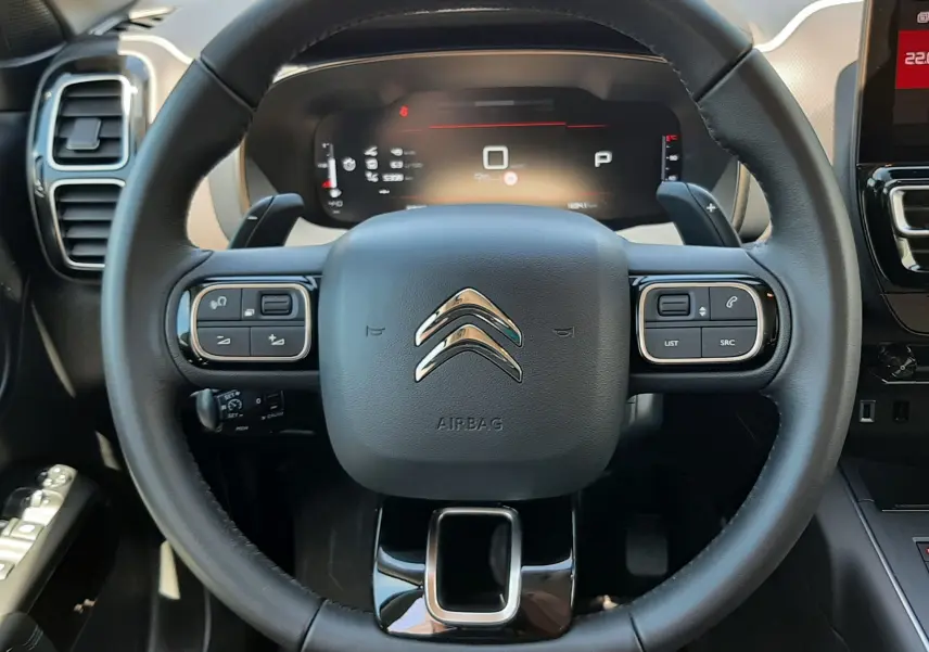 Vue rapprochée du volant noir du Citroën C5 Aircross hybride 2025 avec tableau de bord numérique et commandes intégrées.