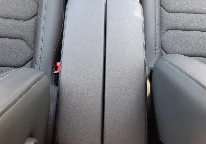 Vue plongeante sur l'accoudoir central noir et les sièges tissu gris foncé de la Citroën C5 Aircross hybride 2025.