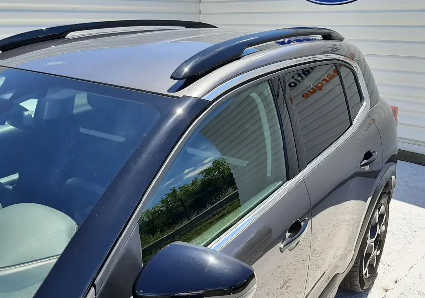 Vue 3/4 avant droit du Citroën C5 Aircross hybride gris platinium avec barres de toit noires et jantes bi-ton.
