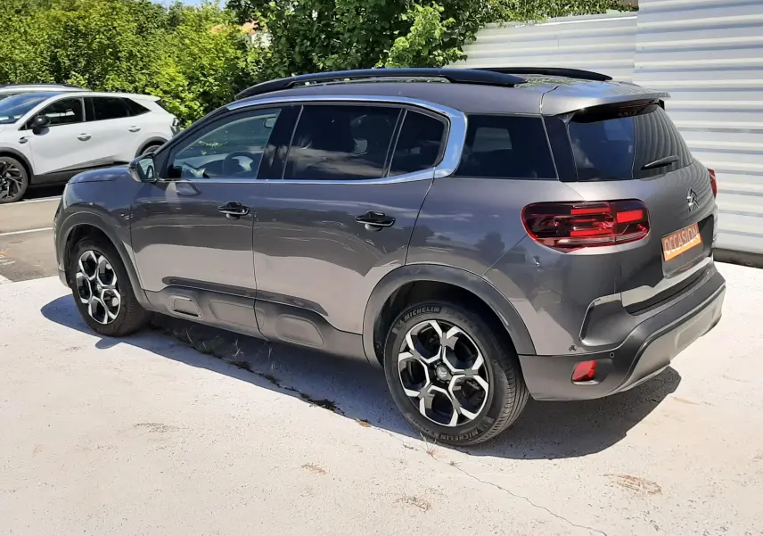 Vue 3/4 arrière droit d'un Citroën C5 Aircross hybride gris platinium avec jantes bicolores et toit noir.