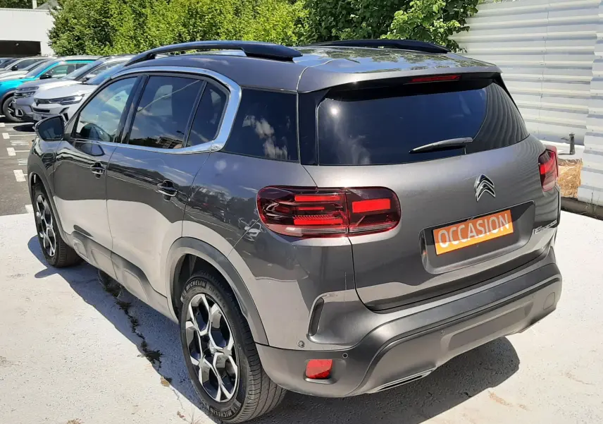 Vue 3/4 arrière droite d’un Citroën C5 Aircross hybride gris platinium avec toit noir et jantes bi-ton.