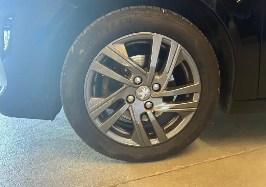 Gros plan sur la roue avant gauche noire d'une Peugeot 208 1.5 BlueHDi 100 Style avec jante alliage grise.