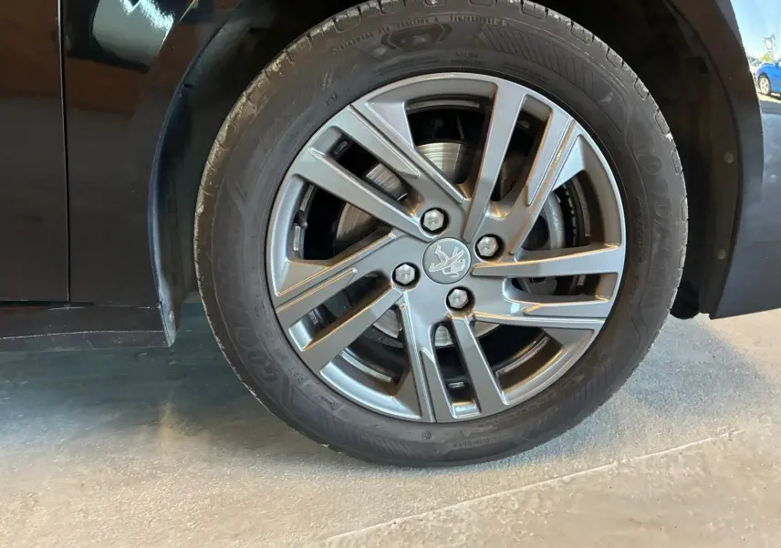 Gros plan sur la roue avant droite d'une Peugeot 208 noire 2021, mettant en valeur la jante alliage au design moderne.