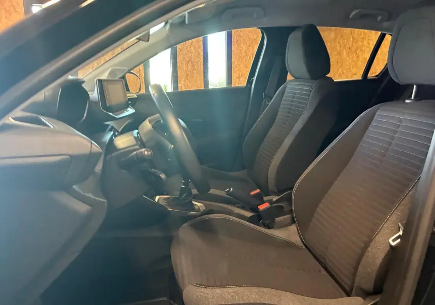Vue intérieure côté conducteur de la Peugeot 208 1.5 BlueHDi 100 Style 2021 avec sièges tissu noirs et tableau de bord moderne.