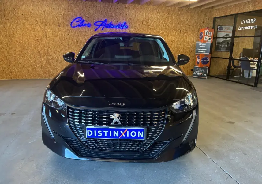 Vue de face d'une Peugeot 208 noire 1.5 BlueHDi 100 Style avec calandre distinctive et plaque Distinxion en intérieur showroom.