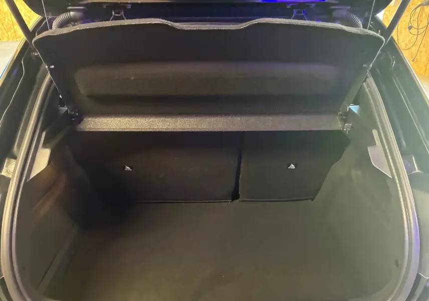 Vue intérieure du coffre ouvert d'une Peugeot 208 noire, montrant un espace de rangement propre et vide.