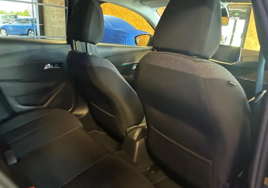 Vue intérieure arrière de la Peugeot 208 noire, montrant les sièges avant en tissu noir et l'habitacle côté droit.