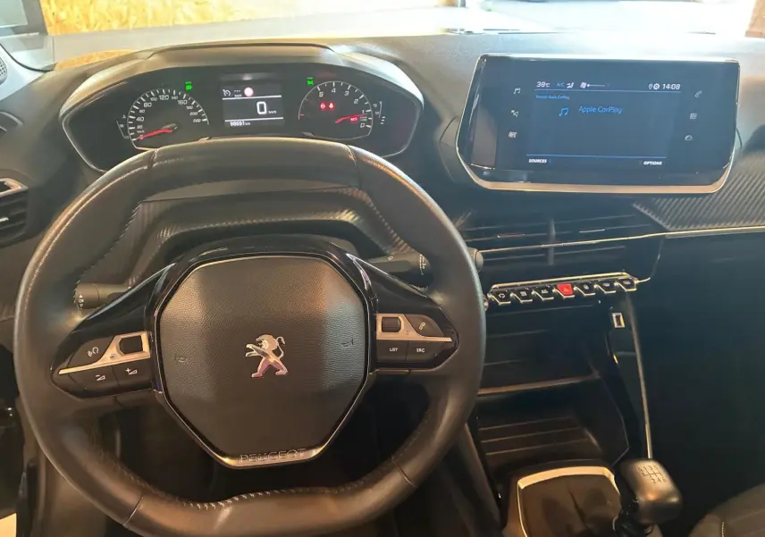 Vue intérieure centrée sur le volant et le tableau de bord de la Peugeot 208 noire avec écran tactile et boîte manuelle.