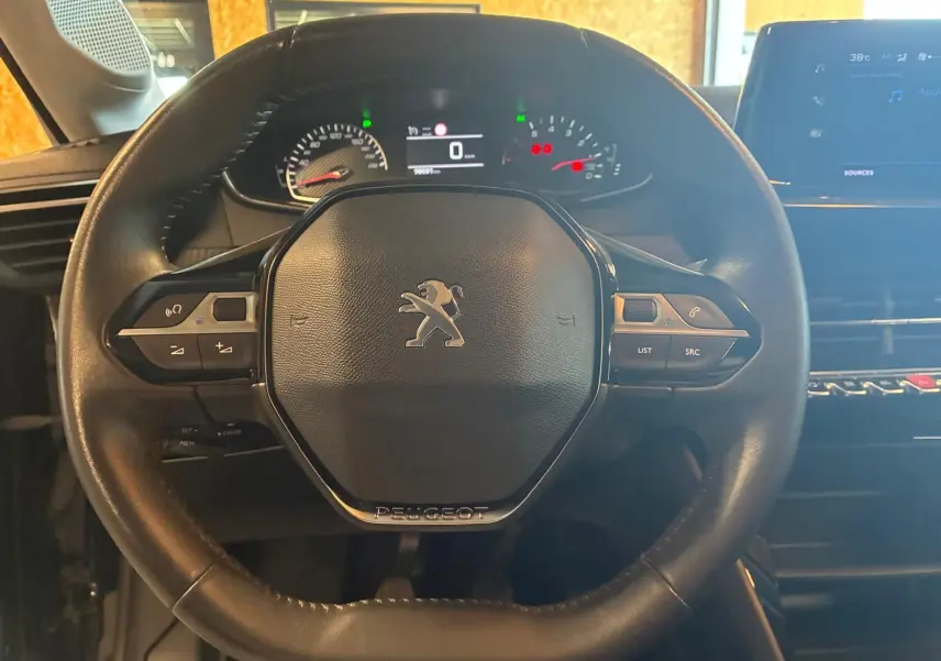 Vue rapprochée du volant noir de la Peugeot 208 1.5 BlueHDi 100 Style avec tableau de bord et écran tactile en arrière-plan.