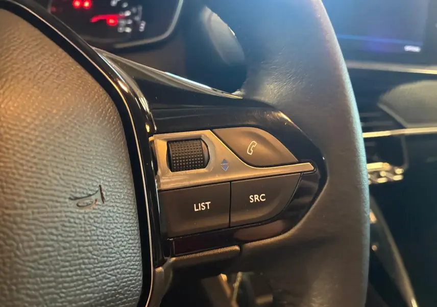 Gros plan sur les commandes gauche du volant noir de la Peugeot 208 1.5 BlueHDi 100 Style, avec boutons LIST et SRC visibles.