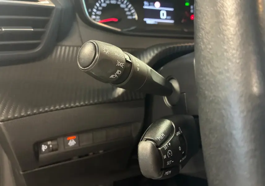 Gros plan sur les commandes de phares et régulateur de vitesse du tableau de bord noir d’une Peugeot 208 1.5 BlueHDi 100 Style 2021.