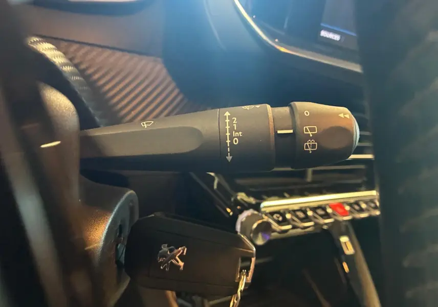 Gros plan sur la manette d’essuie-glace et la clé de contact Peugeot dans l’habitacle noir d’une 208 1.5 BlueHDi.