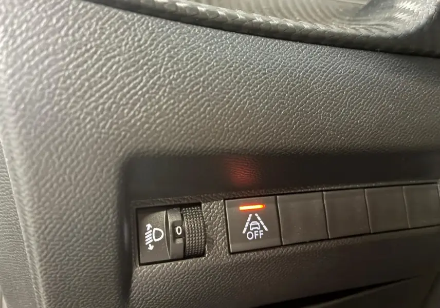 Gros plan sur les commandes noires du tableau de bord d’une Peugeot 208 noire, avec témoin d’alerte allumé.