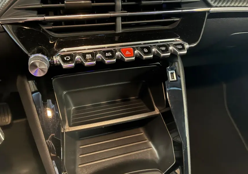 Gros plan sur la console centrale noire du Peugeot 208 1.5 BlueHDi 100 Style 2021 avec boutons de commande et port USB visible.