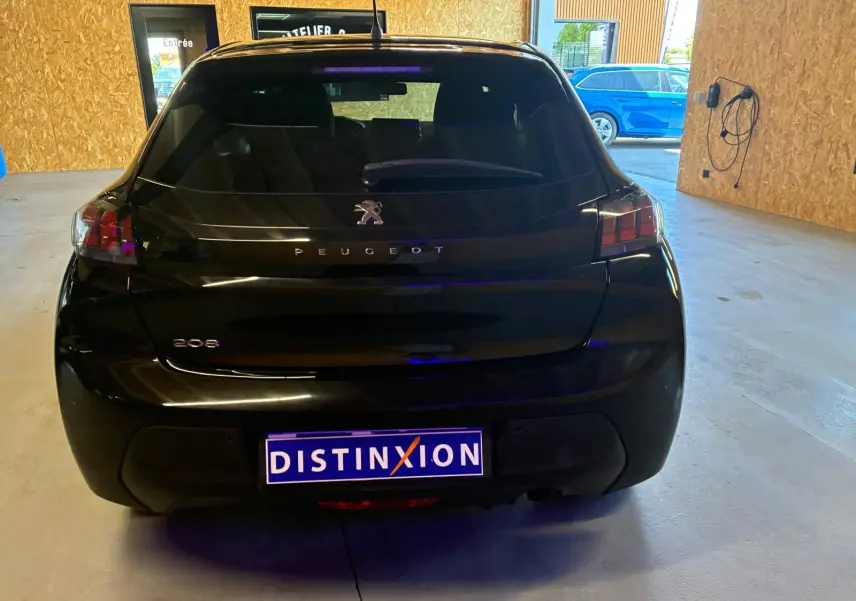 Vue arrière d'une Peugeot 208 noire 2021, avec logo et plaques distinctives visibles en intérieur d'atelier.
