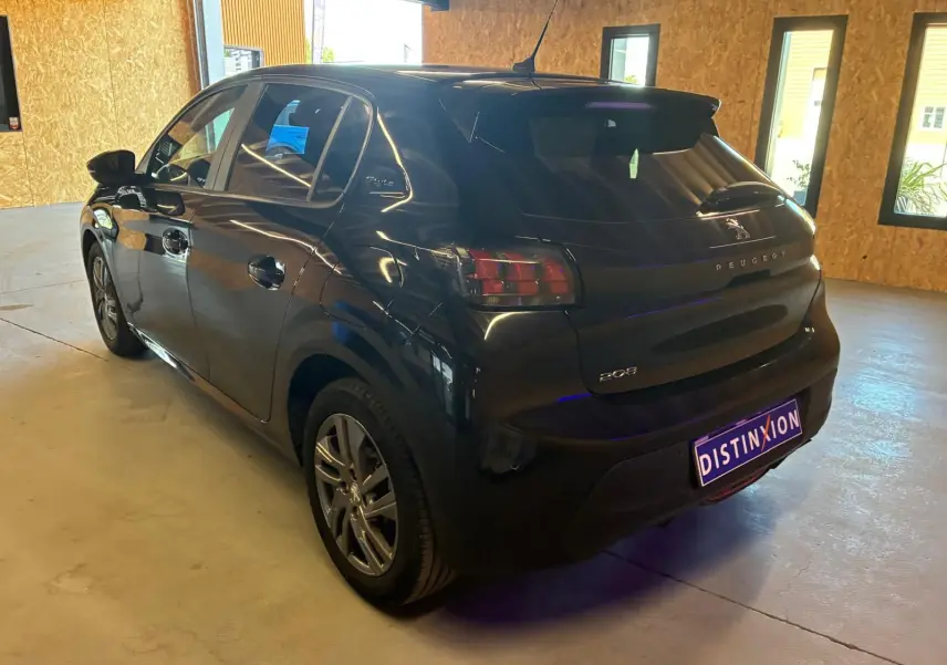 Vue 3/4 arrière droite d'une Peugeot 208 noire 5 portes, stationnée en intérieur avec plaques Distinxion visibles.