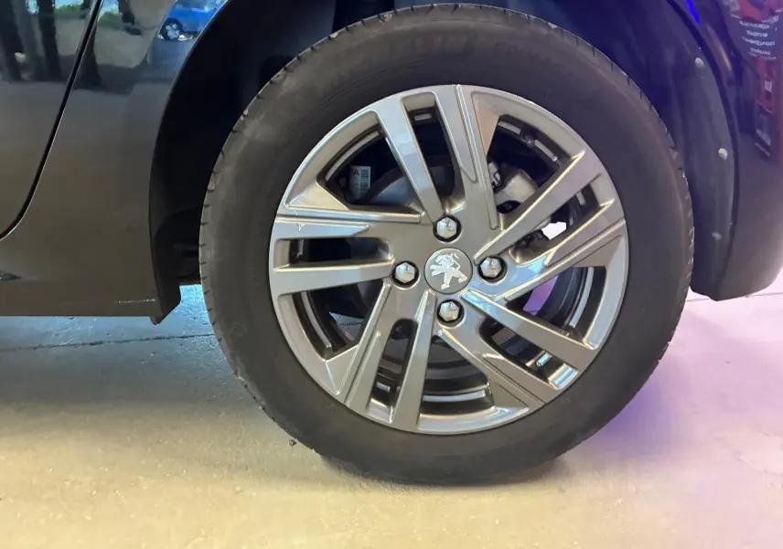 Gros plan sur la roue avant droite noire d'une Peugeot 208 1.5 BlueHDi 100 Style avec jante alliage grise.