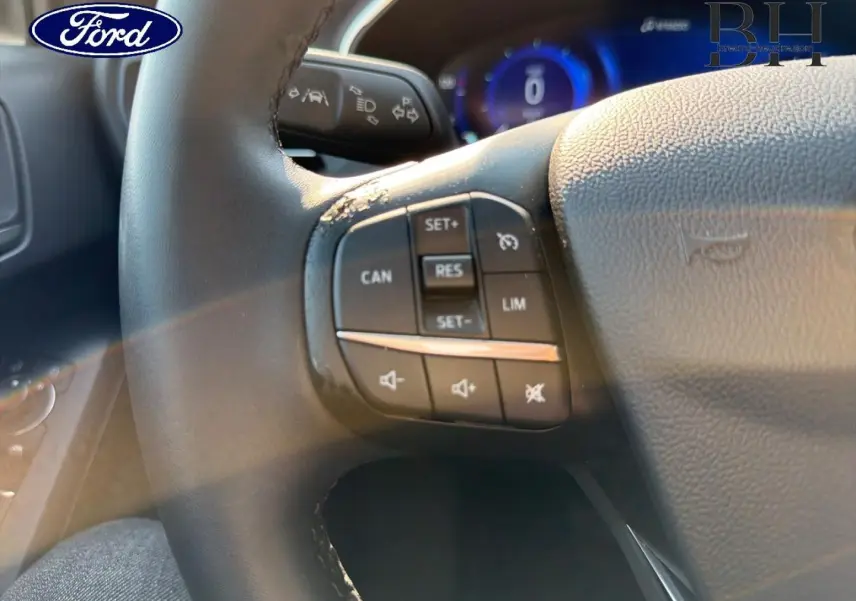 Gros plan sur le volant cuir noir de la Ford Focus 2023 avec commandes multifonctions et tableau de bord numérique bleu.