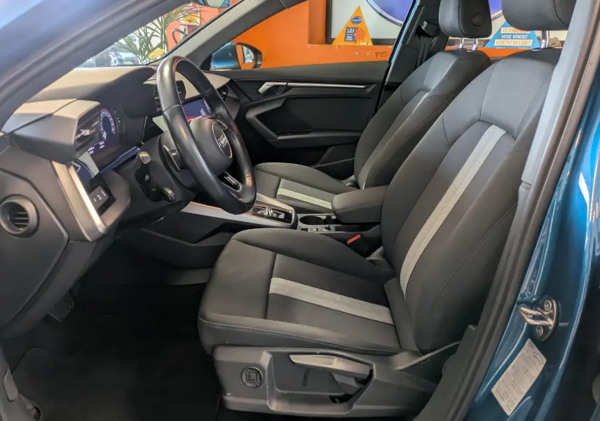 Vue intérieure côté conducteur de l'Audi A3 Sportback bleu Atollblau, montrant sièges et tableau de bord moderne.