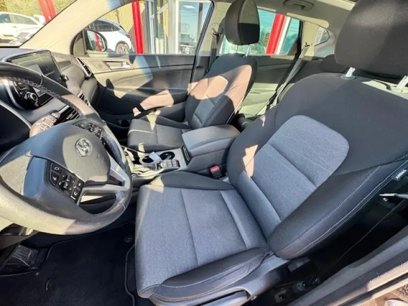 Vue intérieure avant du Hyundai Tucson 2019 avec sièges tissu noir et gris, volant multifonction et console centrale.