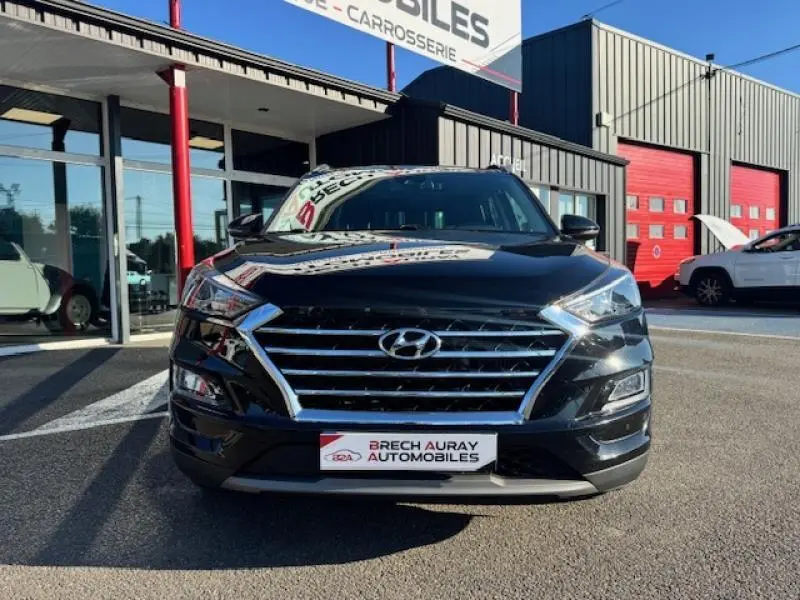 Vue frontale d'un Hyundai Tucson Phantom Black 2019 avec calandre chromée et feux LED, stationné devant un garage.