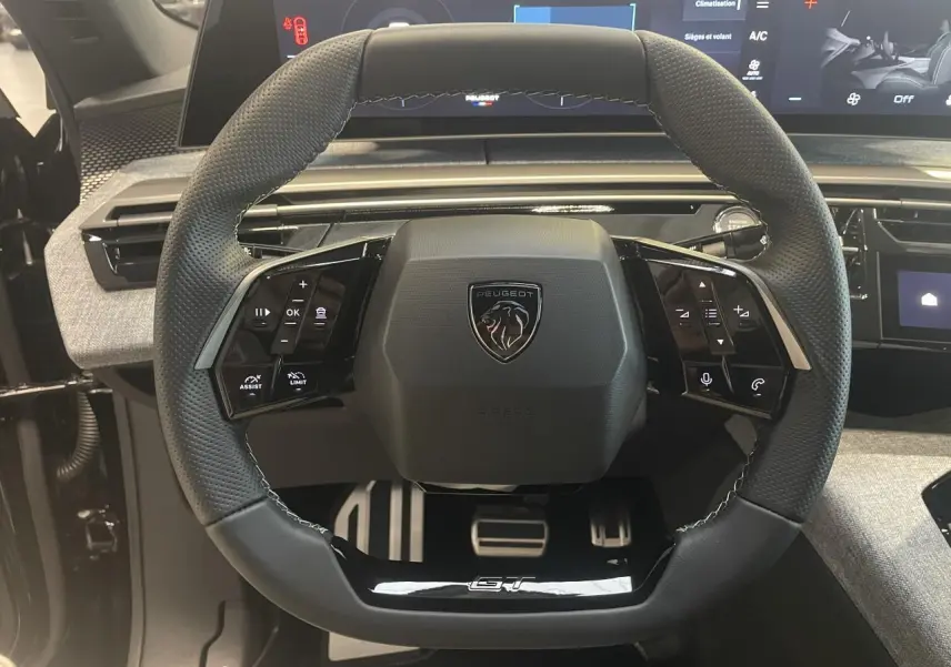 Vue rapprochée du volant compact noir perforé avec logo Peugeot et badge GT du Peugeot 3008 hybride 2025.