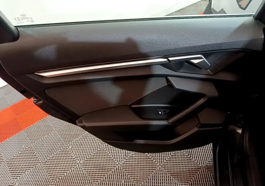 Vue intérieure sur la porte avant gauche de l'Audi A3 gris foncé, avec poignée et commande de vitre intégrée.