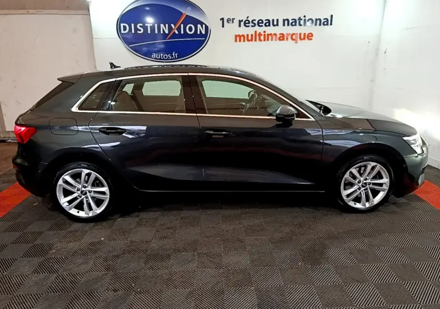 Vue latérale droite d'une Audi A3 35 TFSI gris foncé, en intérieur avec logo Distinxion en arrière-plan.