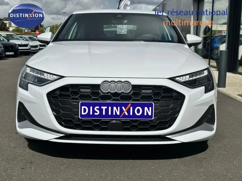 Vue de face d'une Audi A3 Sportback 30 TFSI blanche avec calandre hexagonale noire et logo Distinxion sur plaque avant.