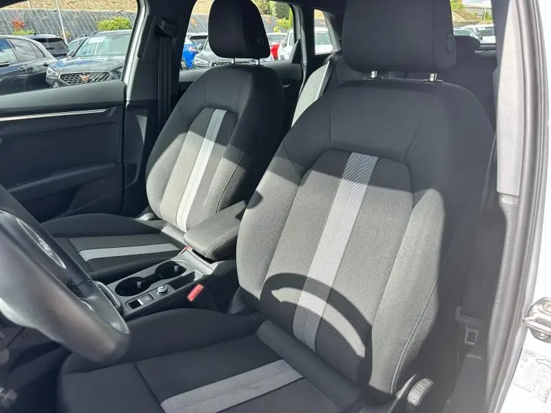 Vue intérieure côté avant droit de l’Audi A3 Sportback 2024, sièges tissu noir avec bande grise centrale et accoudoir.