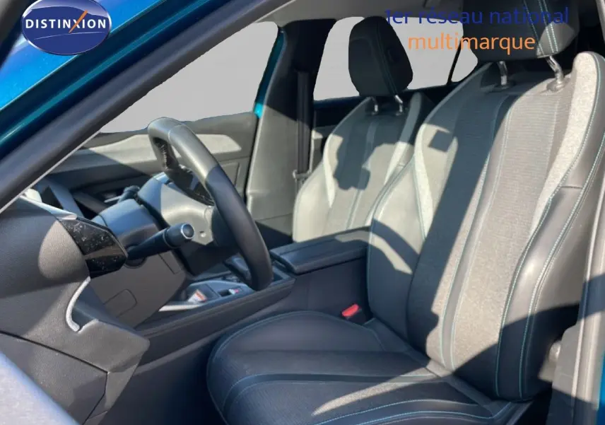 Vue intérieure côté conducteur de la Peugeot 308 2024, sièges tissu et cuir gris noir avec surpiqûres bleues.