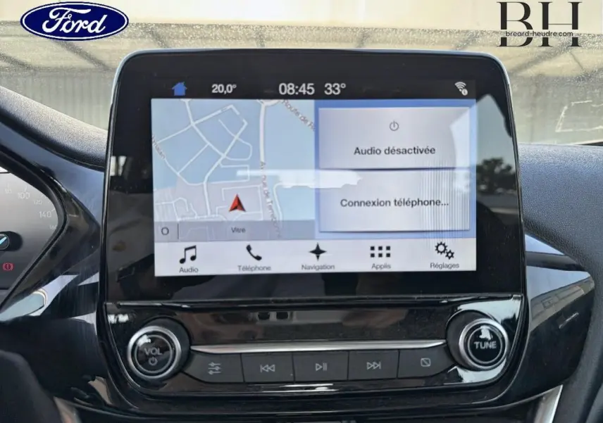 Écran tactile central du tableau de bord de la Ford Fiesta blanc glacier, affichant la navigation et les commandes audio.