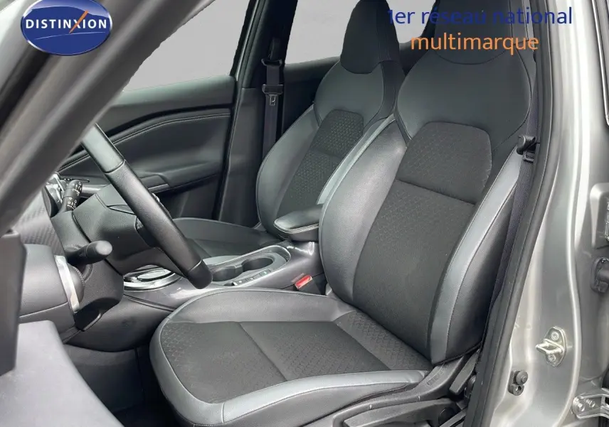 Intérieur du Nissan Juke hybride 2023 en gris perle métal, vue côté conducteur montrant sièges en cuir noir et console centrale.
