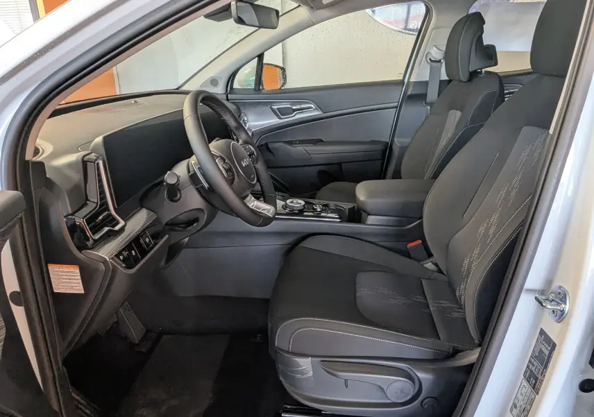 Intérieur côté conducteur du Kia Sportage blanc 2025, sièges noirs avec console centrale et volant multifonctions.