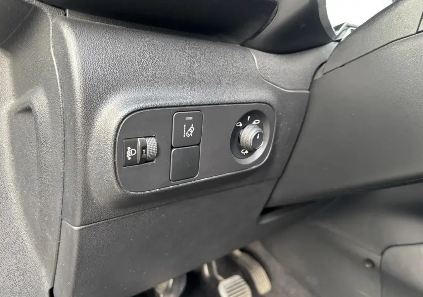 Gros plan sur les commandes de réglage des phares et des rétroviseurs côté conducteur d'une Citroën C3 gris avec toit rouge.