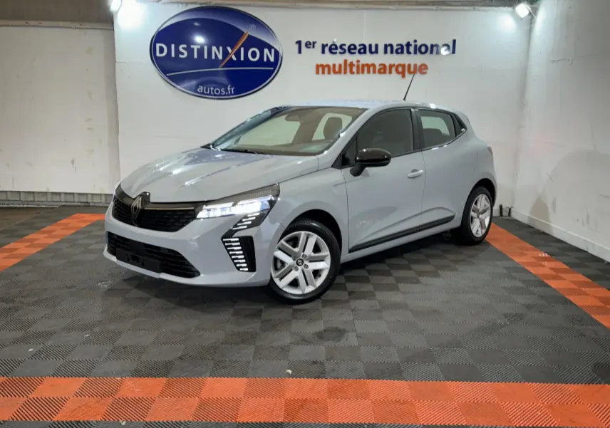 Renault Clio gris clair vue 3/4 avant droit, avec feux LED allumés et jantes alliage, en intérieur showroom.