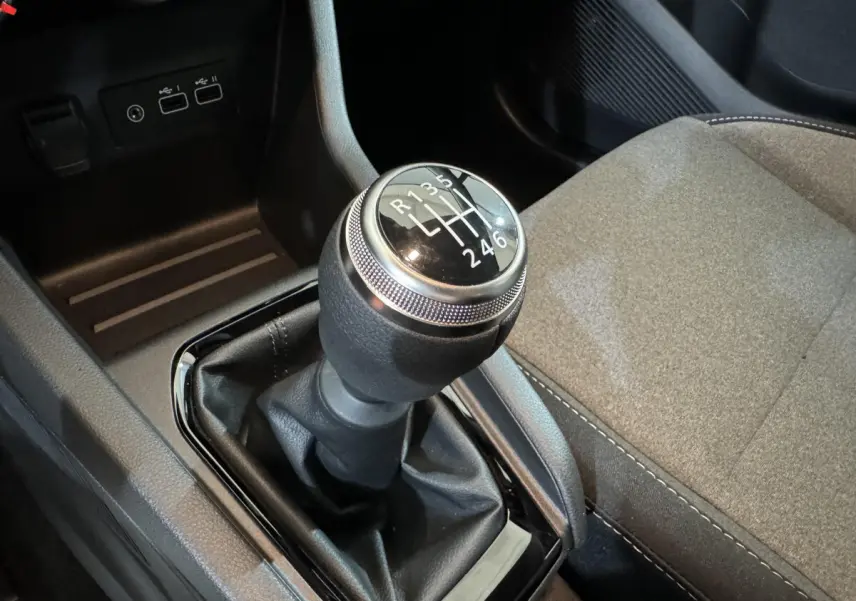 Gros plan sur le levier de vitesses manuel noir et argenté de la Renault Clio gris clair, avec siège tissu beige visible à droite.