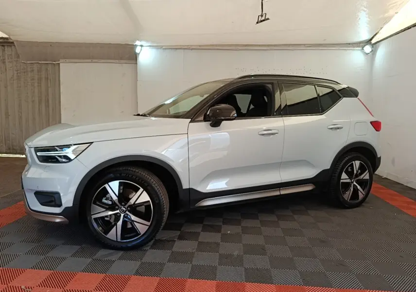 Vue de profil côté gauche d'un Volvo XC40 P8 R-Design gris clair dans un garage avec jantes noires et toit noir.
