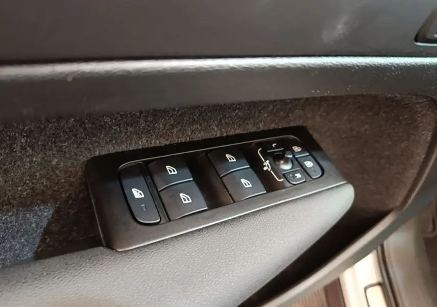 Gros plan sur les commandes de lève-vitres et rétroviseurs côté conducteur du Volvo XC40 gris clair électrique.