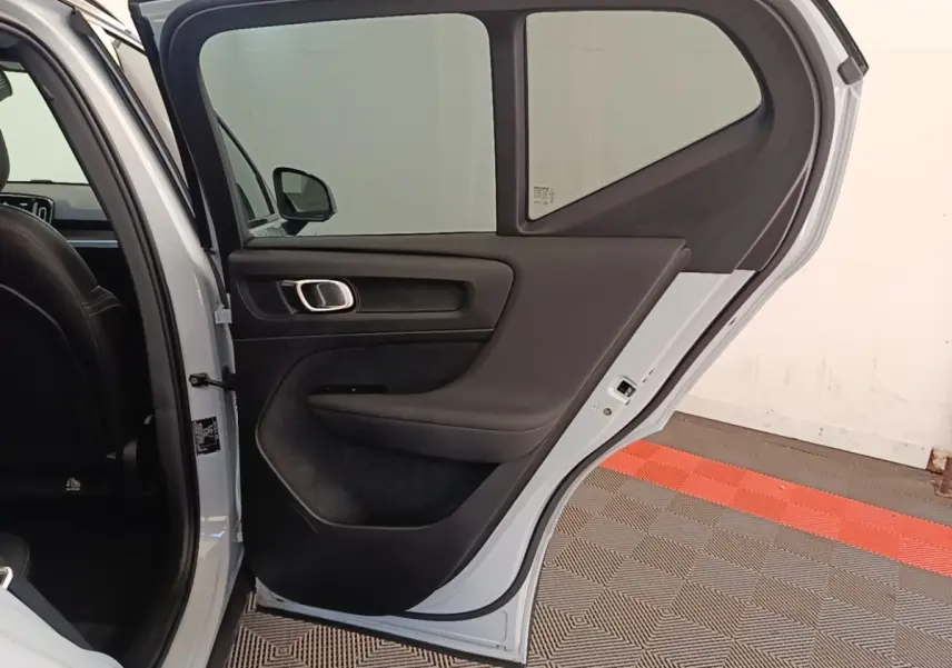 Vue intérieure de la porte arrière gauche ouverte d’un Volvo XC40 gris clair, avec garniture noire et poignée argentée.